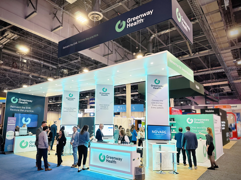 a picture of a tradeshow booth for Greenway Health with Green, white and darkblue accents, along with touchscreen TV's and people walking around